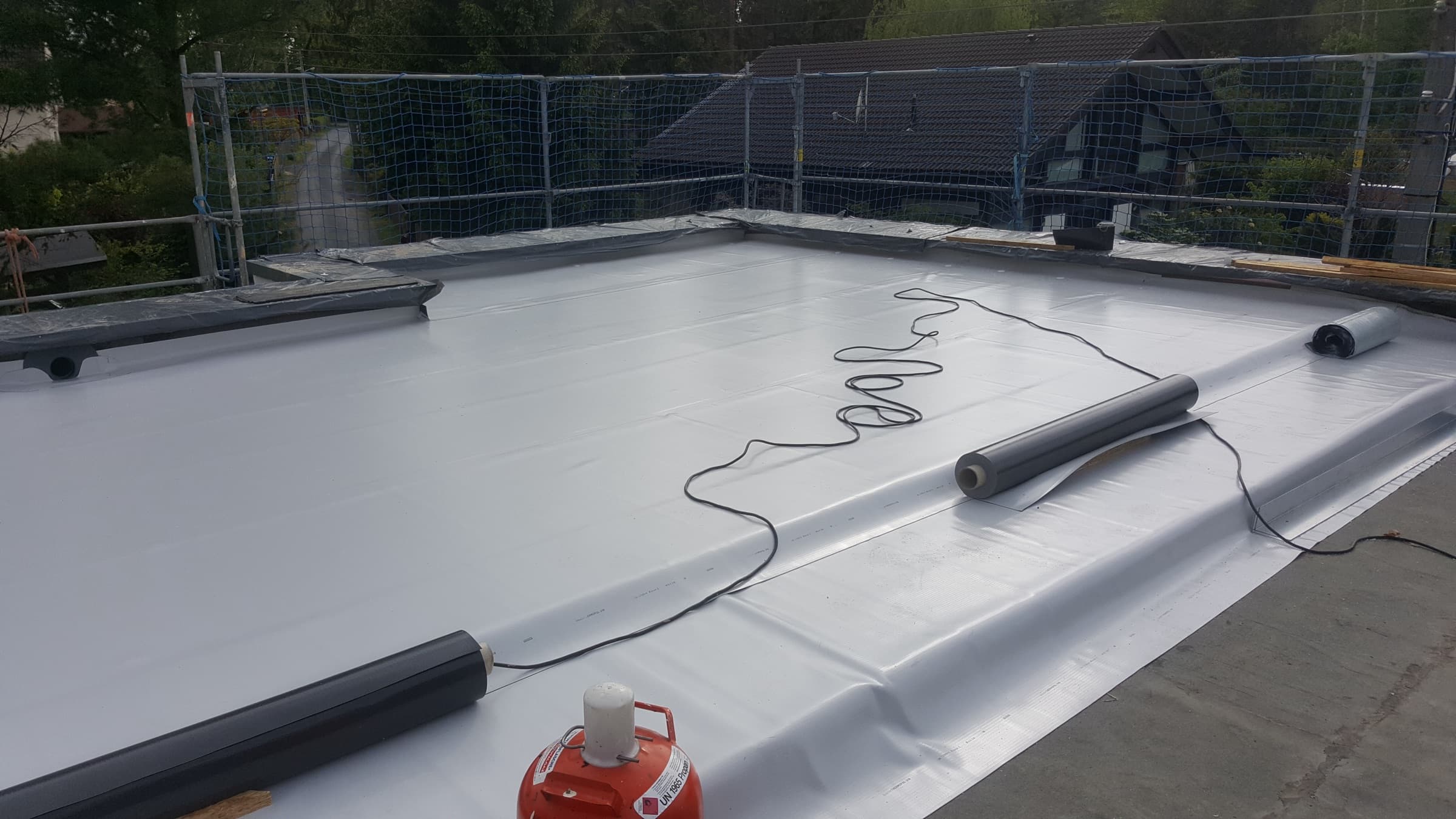 White single-ply roofing membrane rolled out across a flat roof during installation