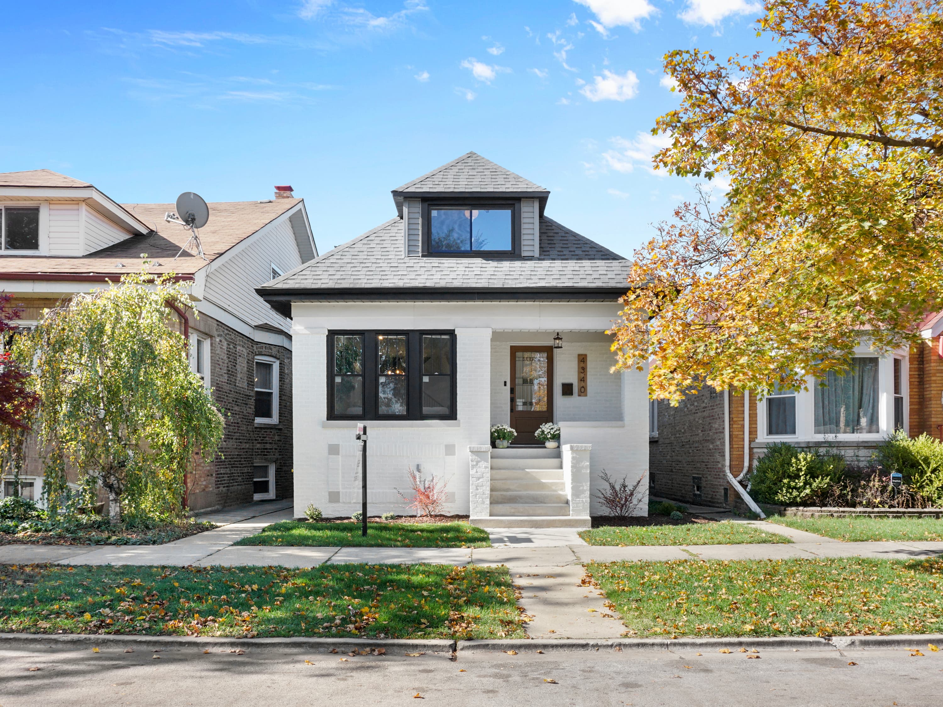 A renovated white brick bungalow with a new roof and dormer window
