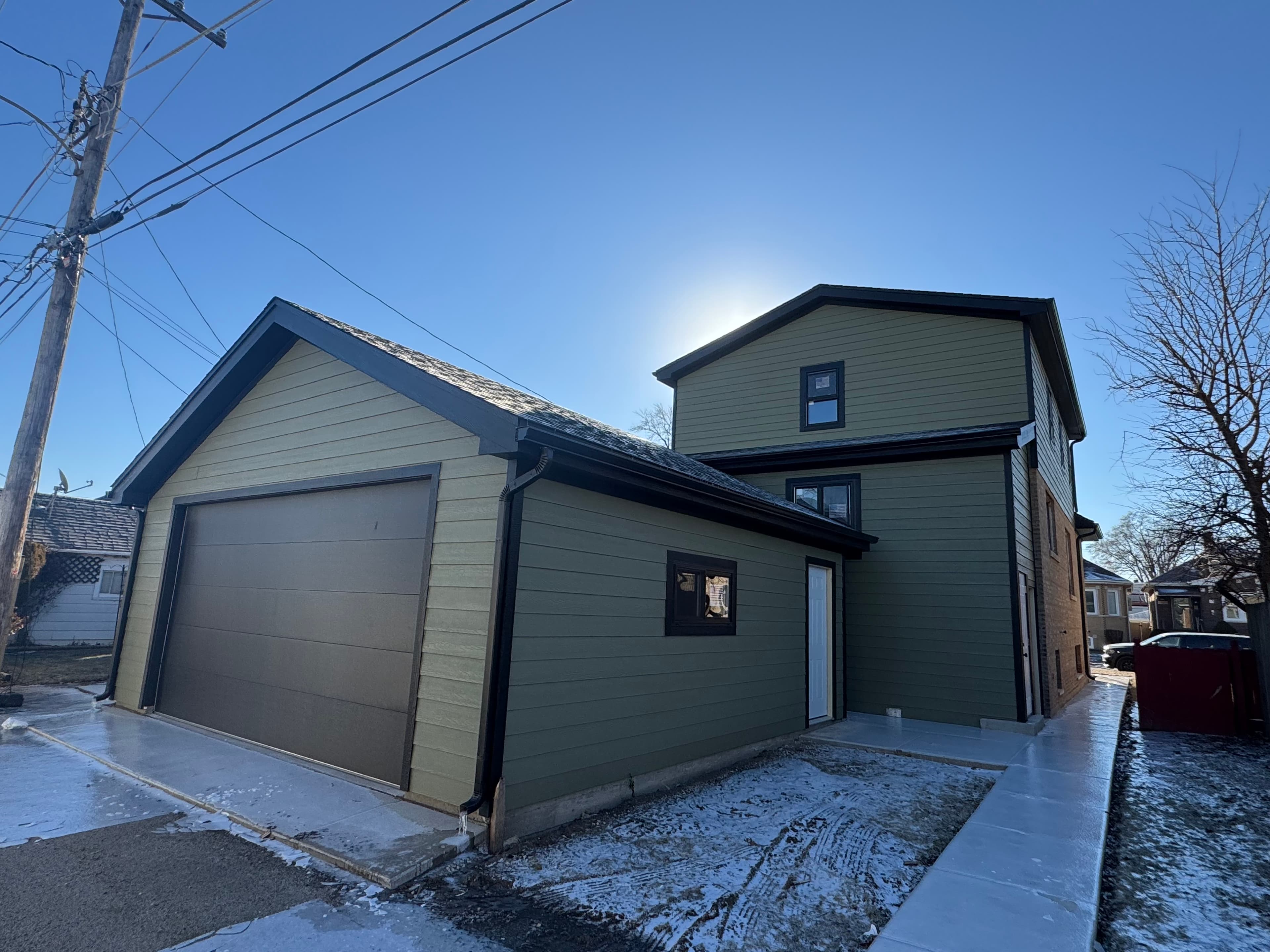 Renovated home and garage with green lap siding, black trim, new shingles, and black gutters