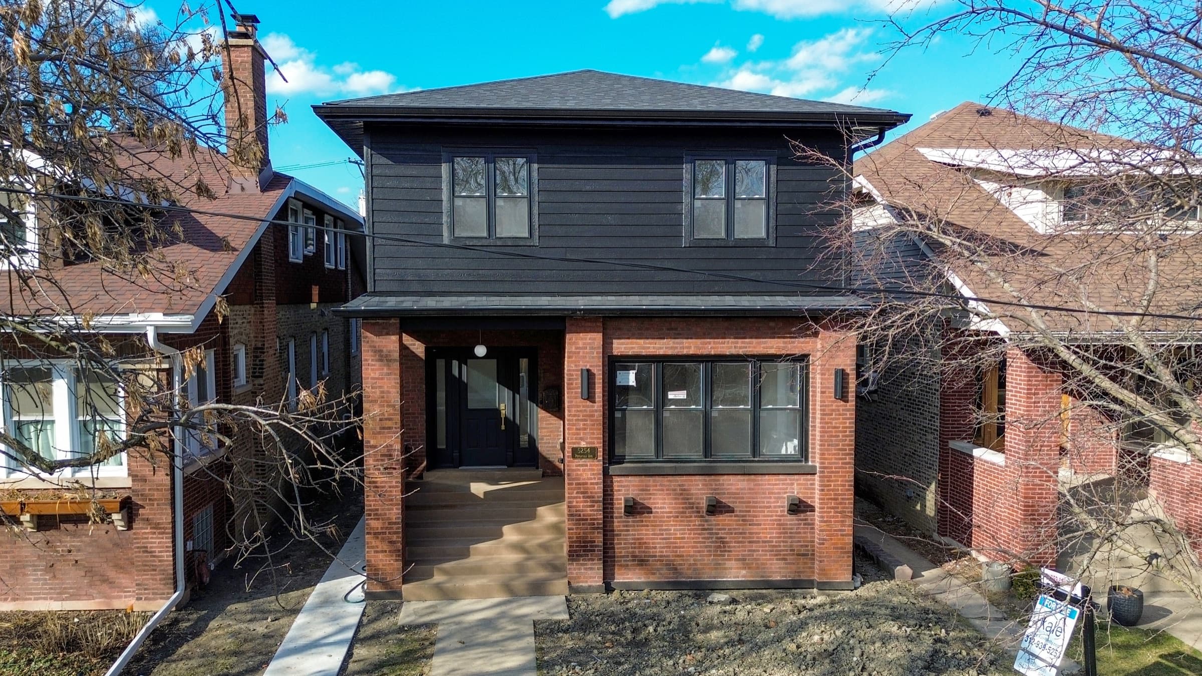 Front of a renovated two-story brick home with new black horizontal siding, black windows, and a dark shingle roof