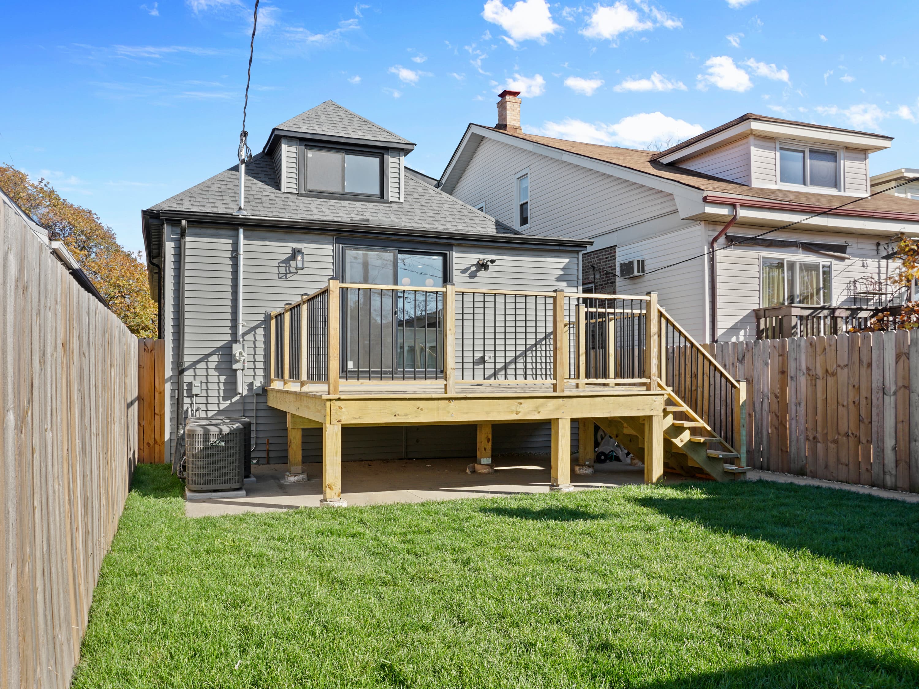 Rear of a renovated home with new gray siding, shingle roof and dormer, and a new wood deck with black railings