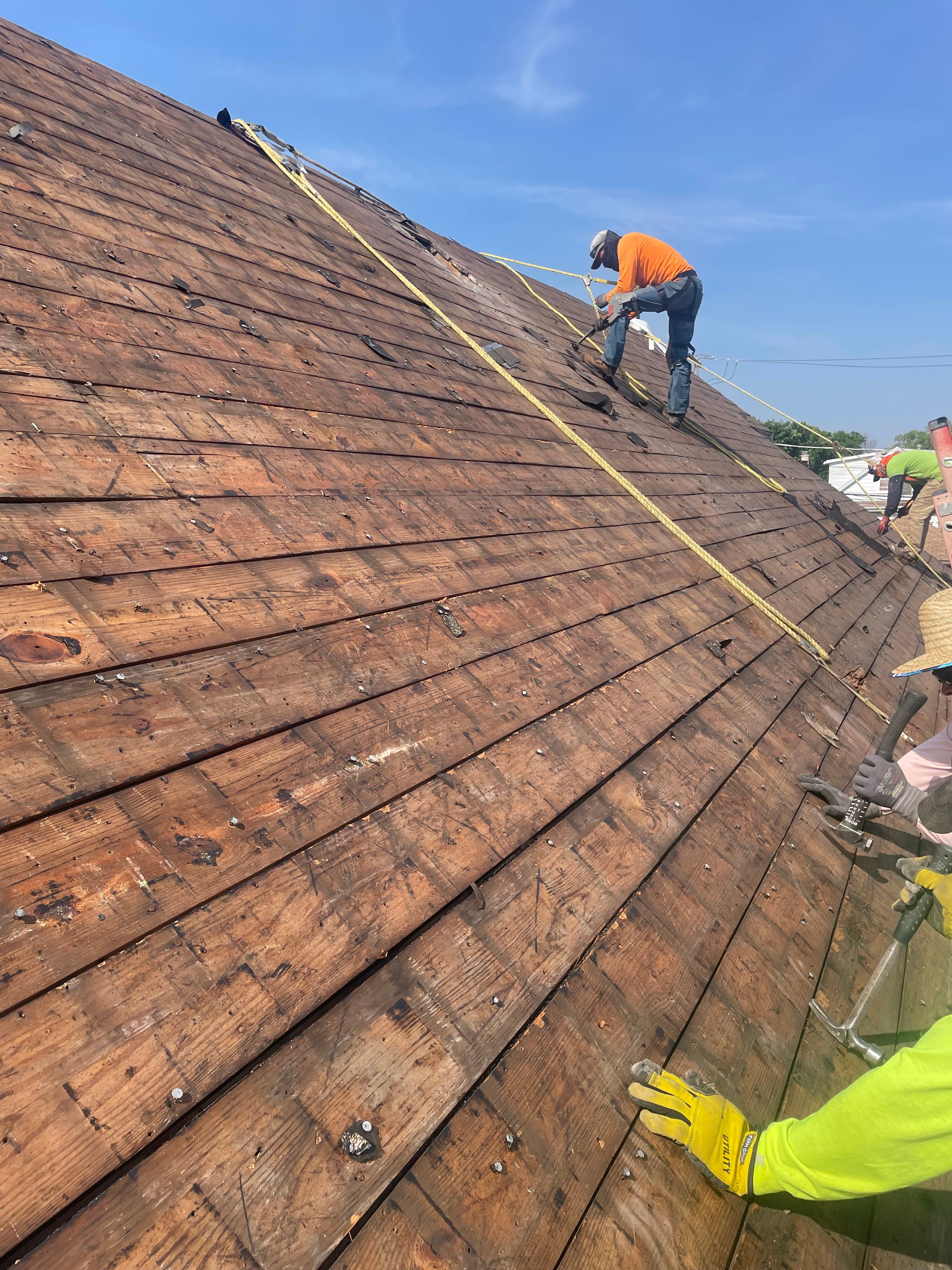 Roofing crew on a bare roof deck during tear-off, tied off with safety lines