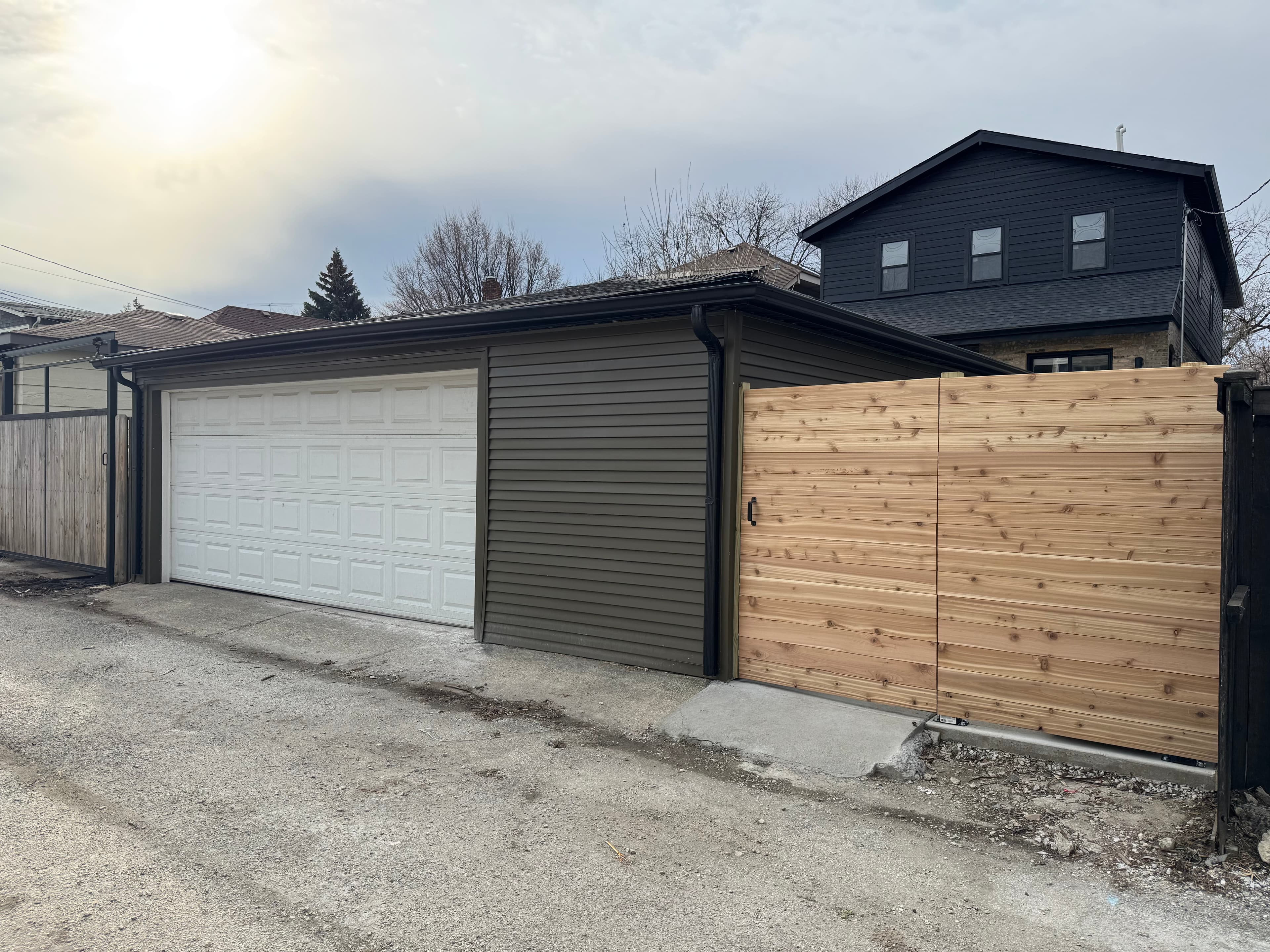 Alley garage with new siding, black gutters and downspouts, and a cedar gate beside a renovated home