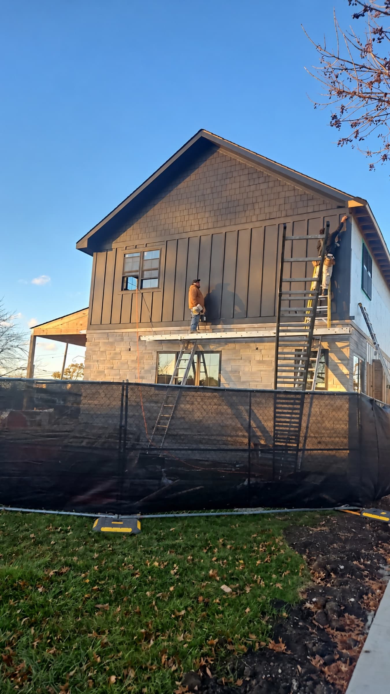 Crew installing dark board-and-batten and shingle-style siding above a stone base on a new two-story home