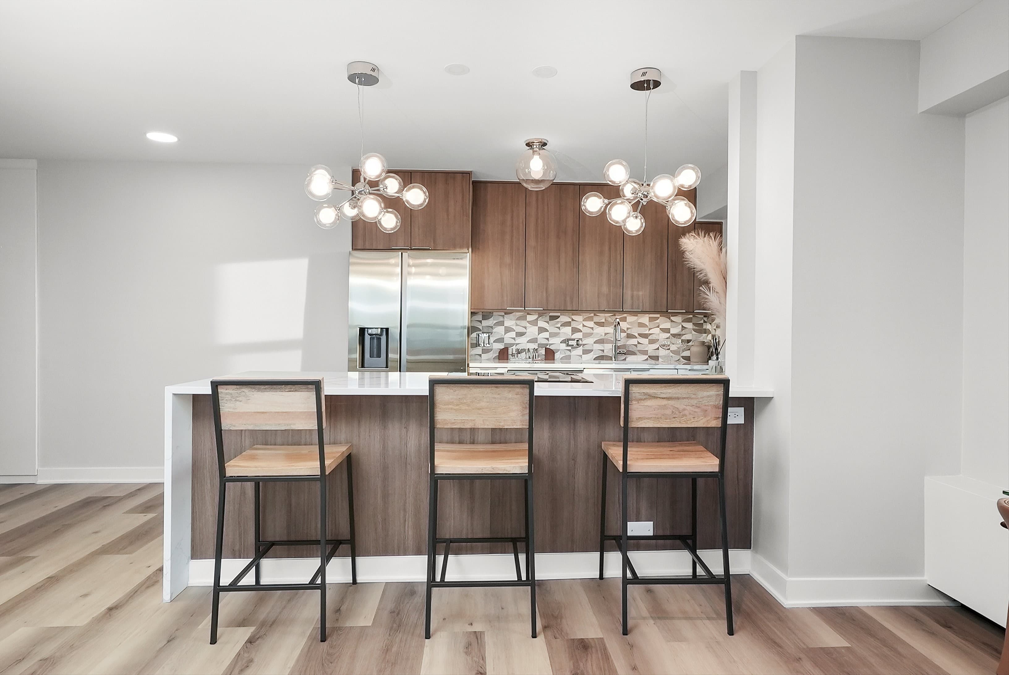 A straight-on view of the renovated kitchen with wood-tone cabinets and bar stools