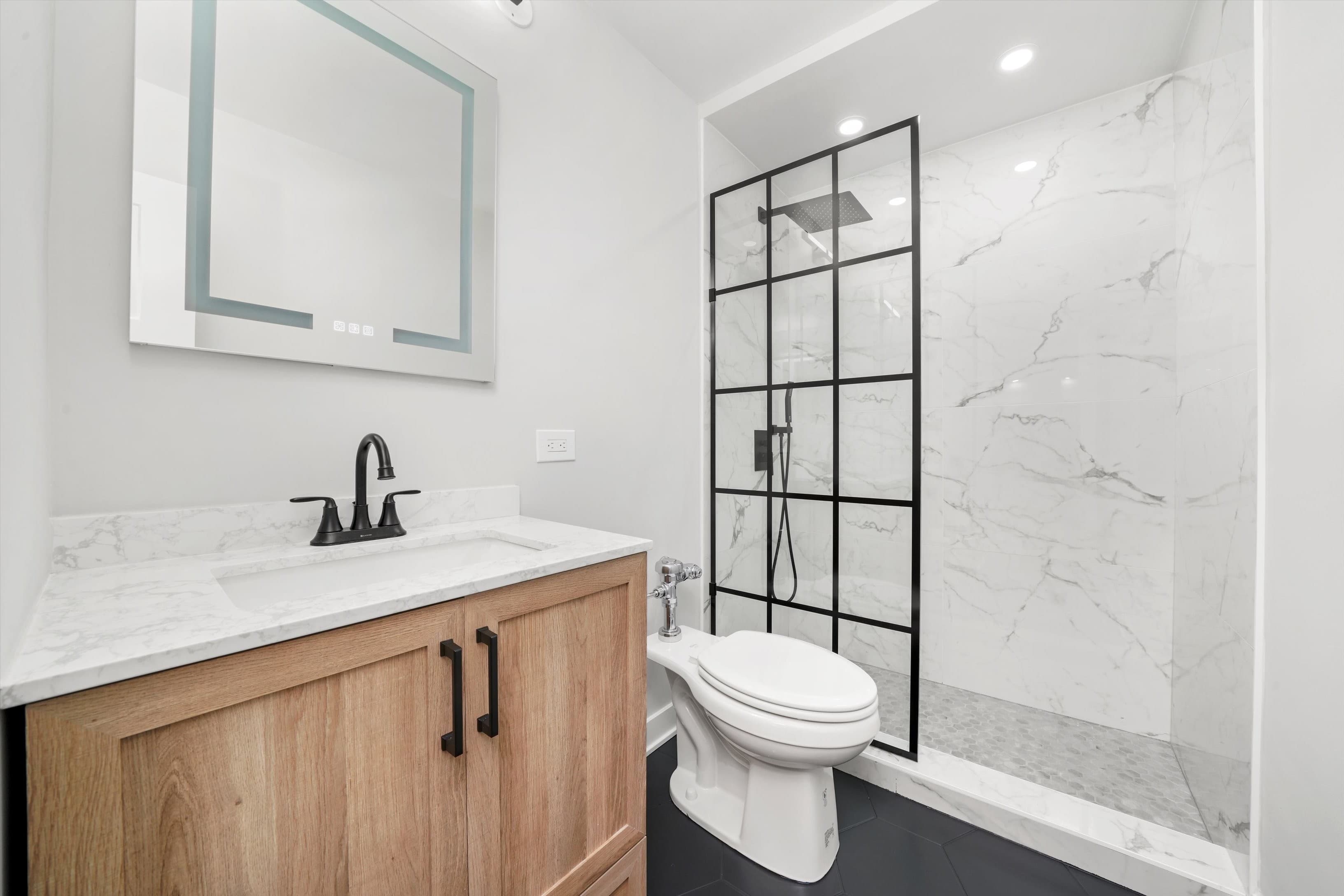A renovated bathroom with a black-grid glass shower