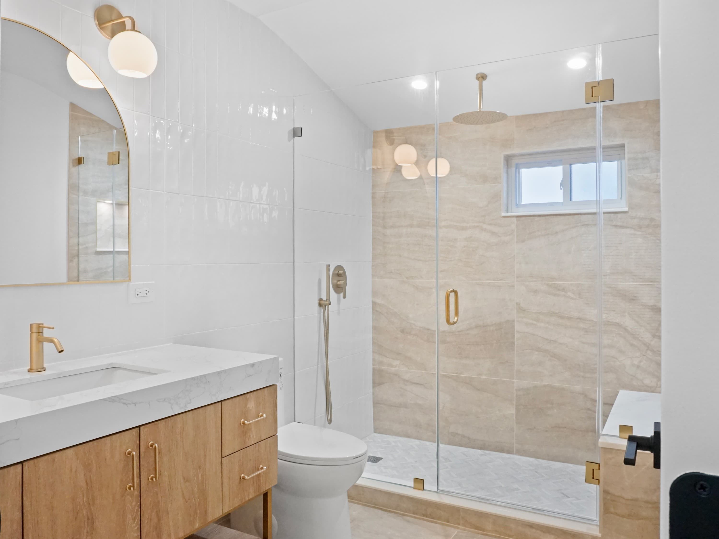 A renovated bathroom with a walk-in glass shower and stone-look tile
