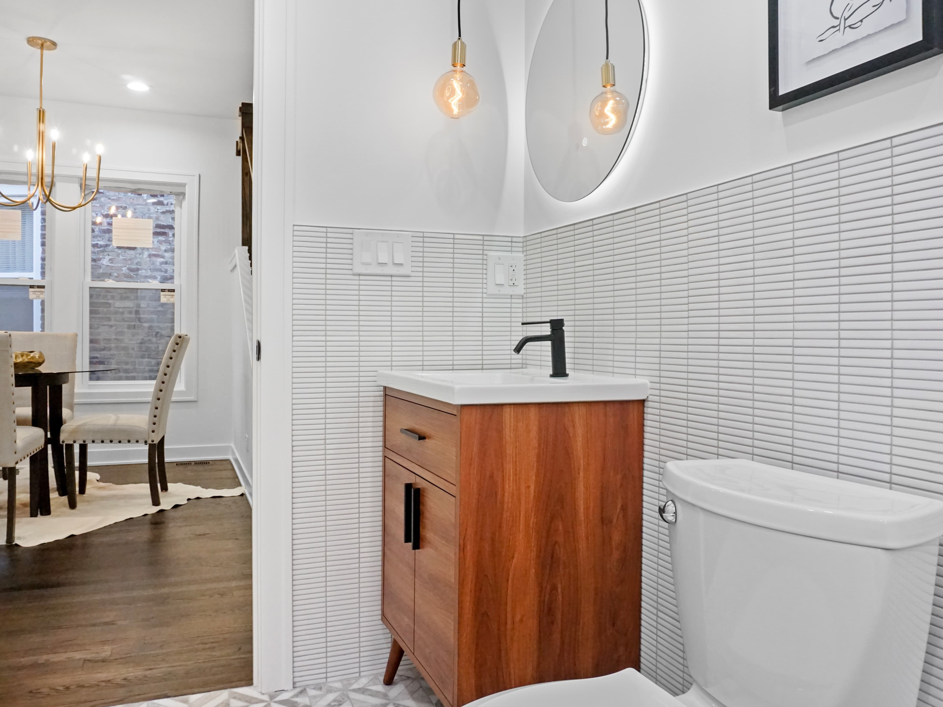 A compact modern powder room with a round backlit mirror and patterned floor tile