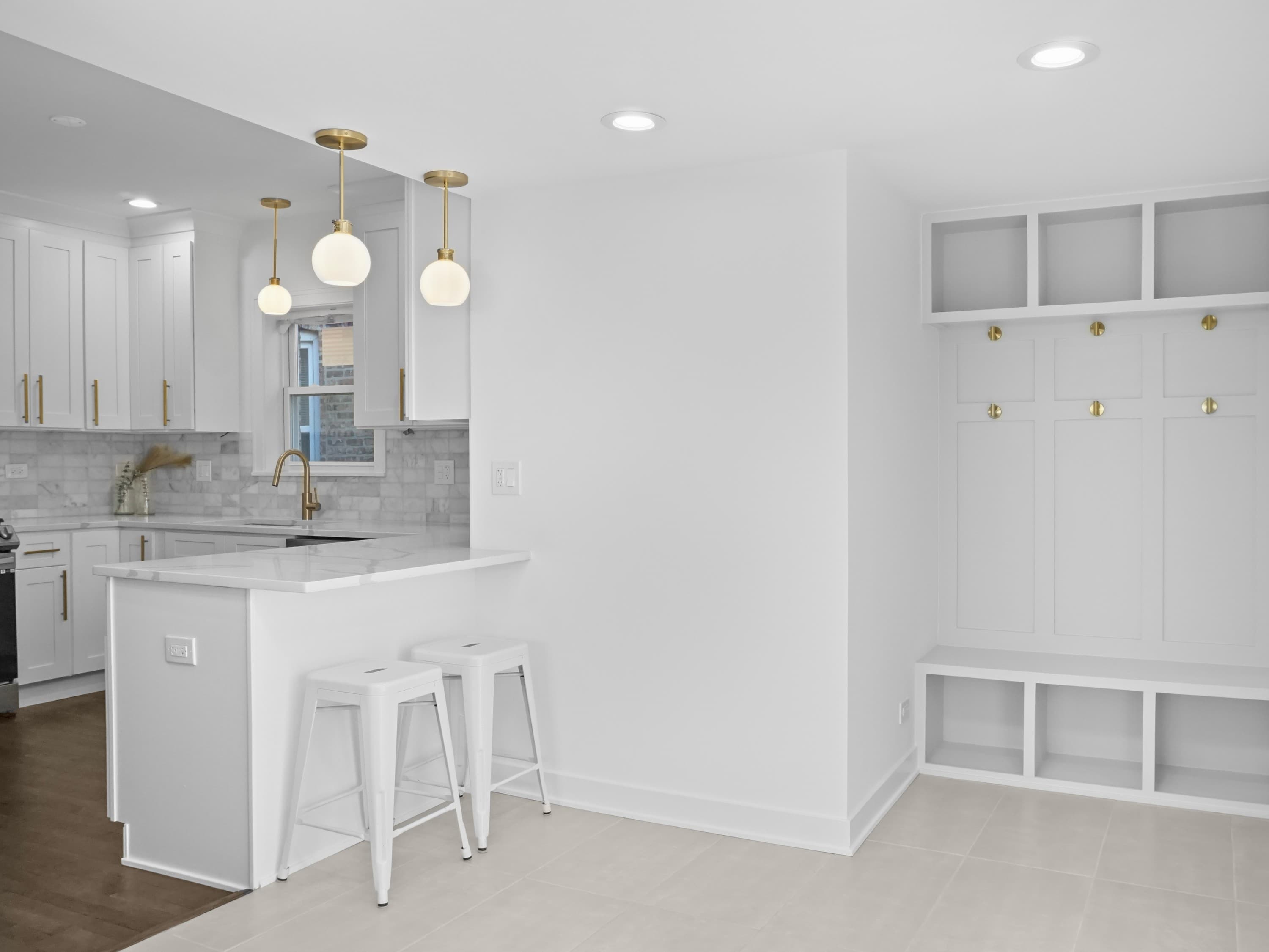 A kitchen peninsula with white cabinetry and gold pendant lights