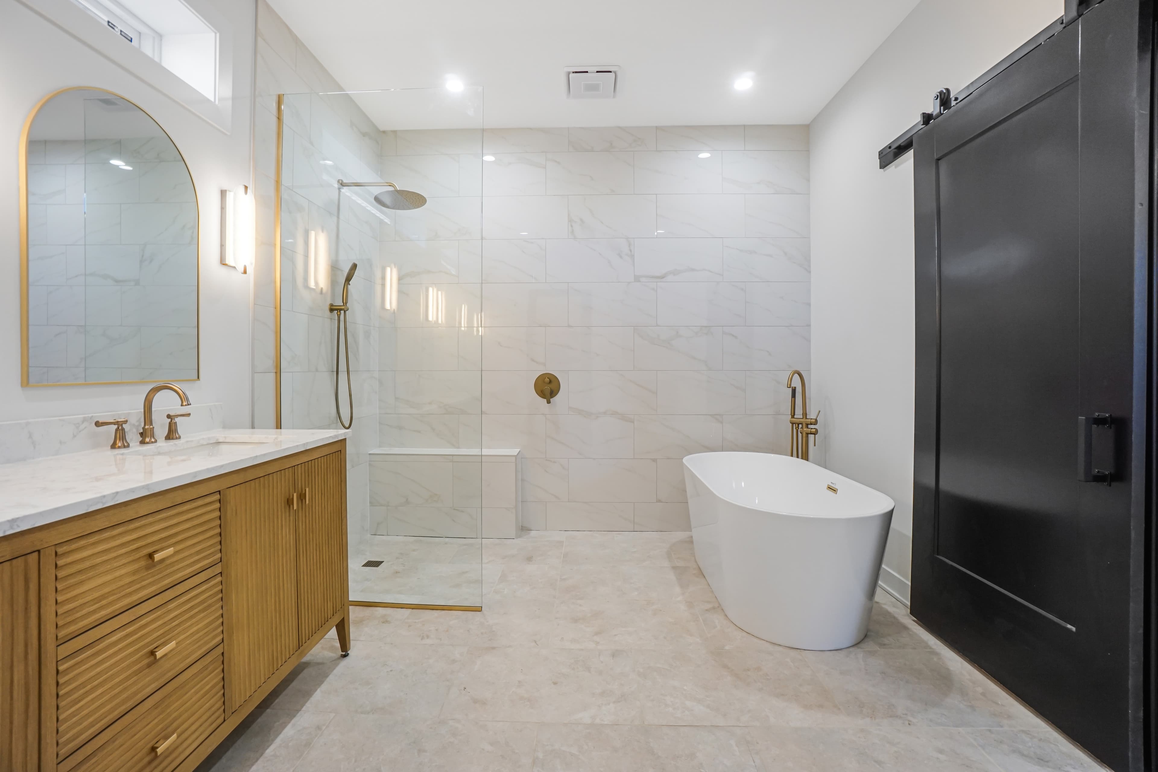 The vanity and glass walk-in shower with gold fixtures and a sliding barn door