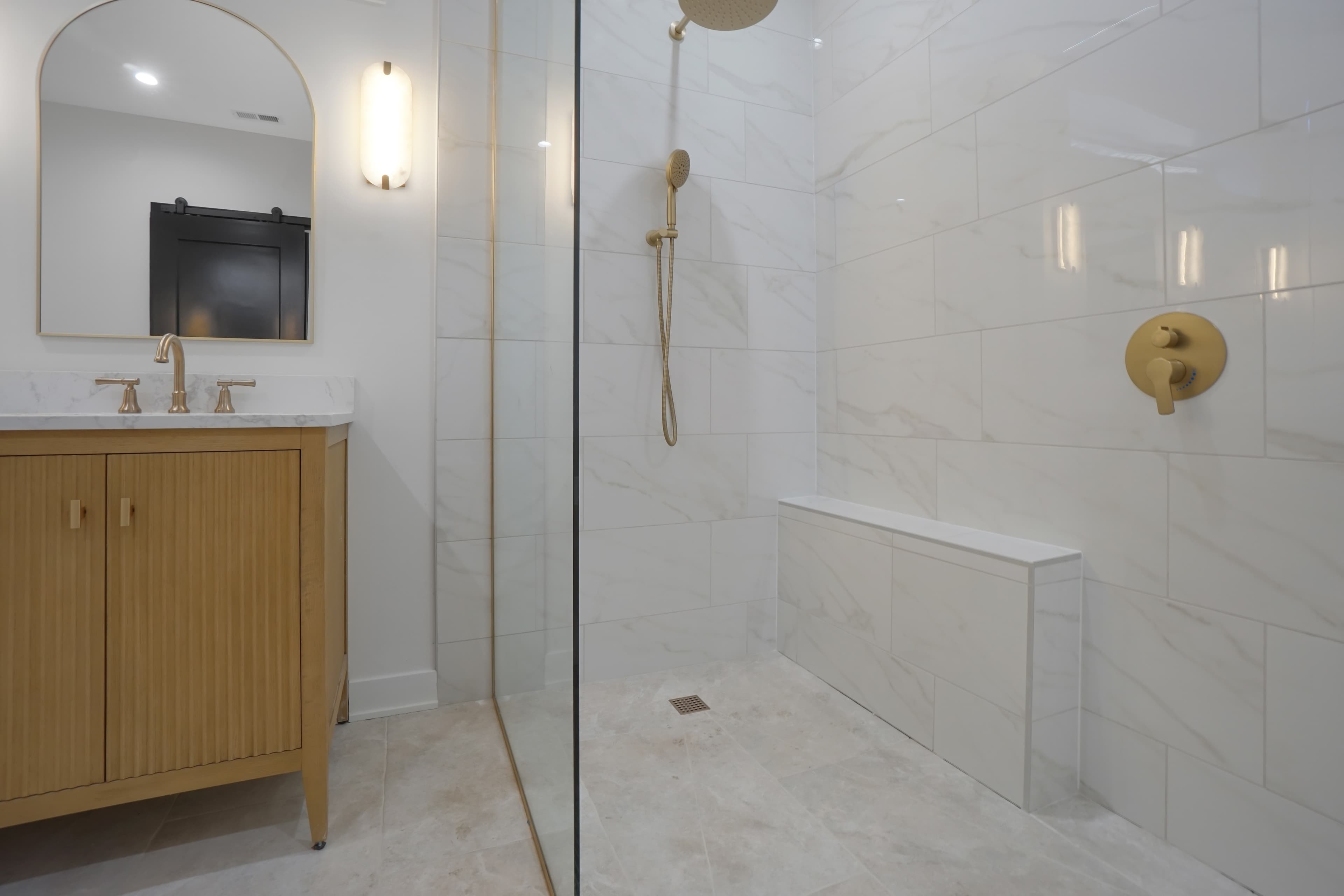 A close view of the glass walk-in shower with a gold rain shower head and handheld sprayer
