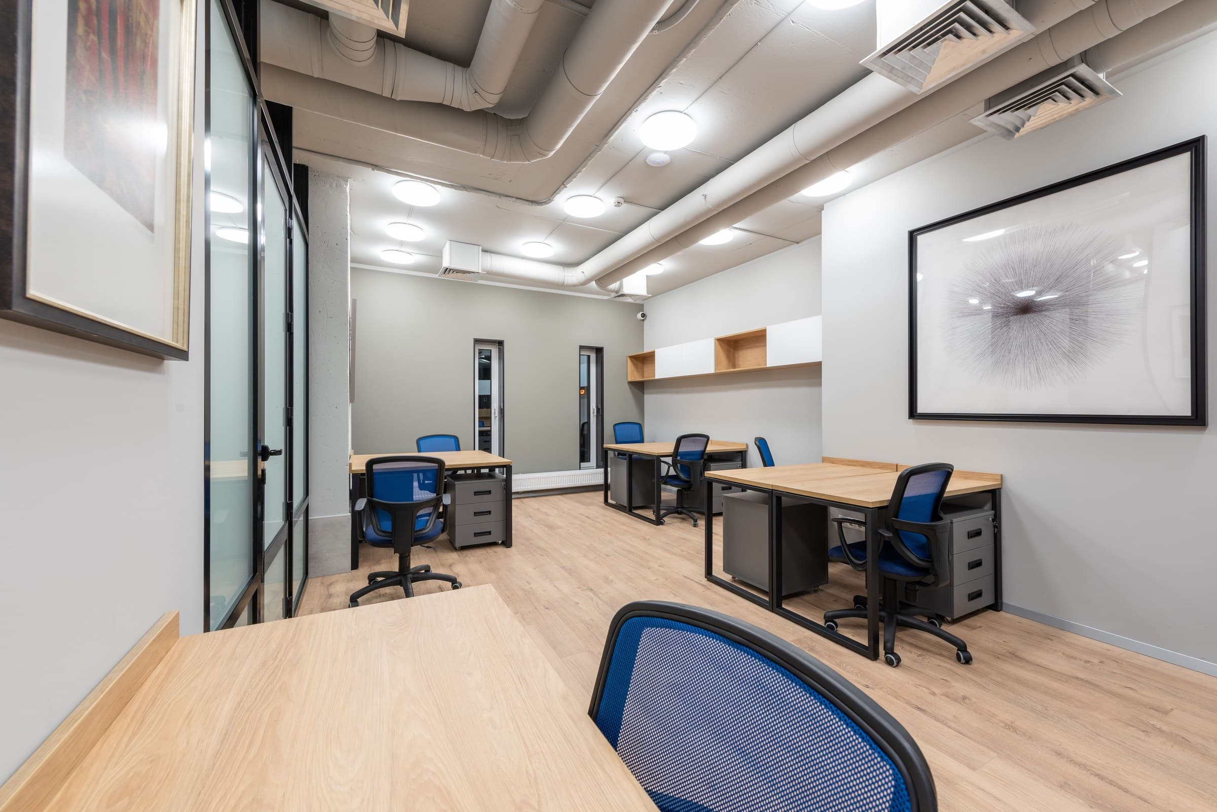A finished commercial office with wood desks, glass partitions, and exposed ceiling ductwork